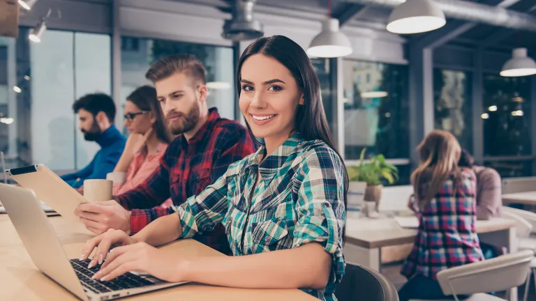 Two women and two men sit next to each other at a table and look at laptops and tablets.