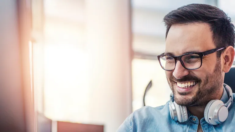 Lachender Mann mit Brille und Dreitagebart schaut lachend auf Bildschirm und tippt auf Tastatur.