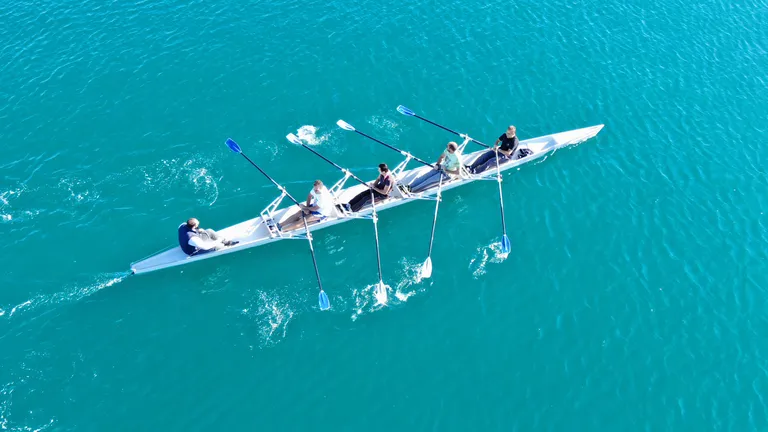 View from above of 5 people in a rowing boat on the water 4 people rowing.