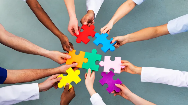 Twelve hands hold seven differently coloured puzzle pieces in the middle.