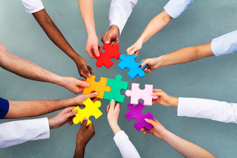Twelve hands hold seven differently coloured puzzle pieces in the middle.