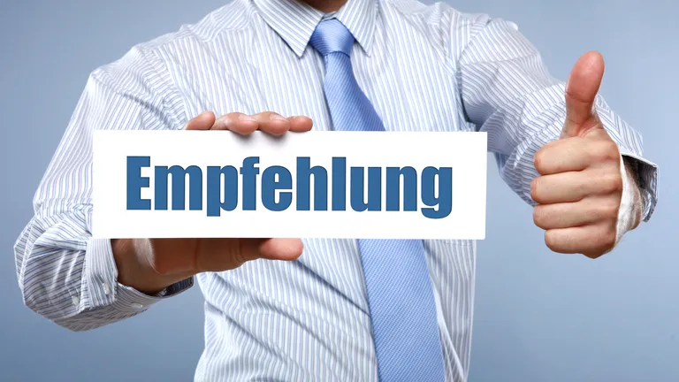 Mann in einem gestreiften Hemd hät ein Zeichen auf dem Empfehlung steht und streckt den linken Daumen hoch.