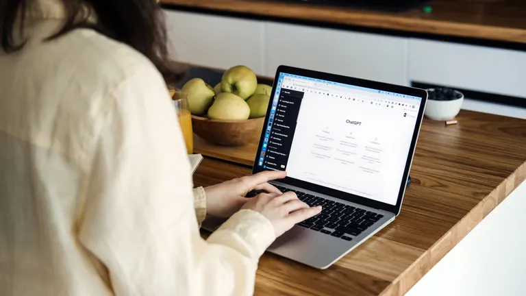 Woman sitting with laptop at the table on the laptop you can see ChatGPT open.