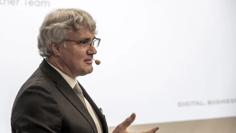 Hanspeter Himmel in a suit and with a microphone in front of a screen.