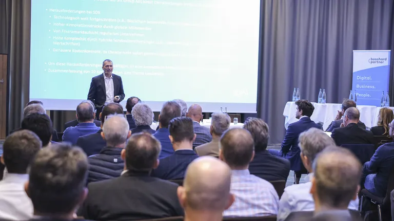 Publikum am Keynote-Event 2023 von hinten, vorne steht einer der Referenten und spricht zum Publikum.