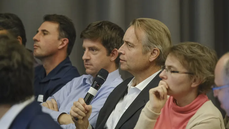 Various guests from the 2023 keynote event sit next to each other, the man in the centre holds a microphone.