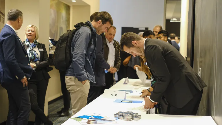 Guest reception at the 2023 keynote event Bosshard & Partner employees stand behind a white table and hand out name labels to guests.