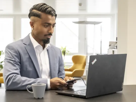 Jenushan Vijayaratnam, an employee of Bosshard & Partner, is standing at a high table, holding a calculator in his hand and looking at his laptop.