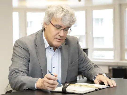 Hanspeter Himmel, an employee of Bosshard & Partner, stands at a high table and writes something in the notebook in front of him.