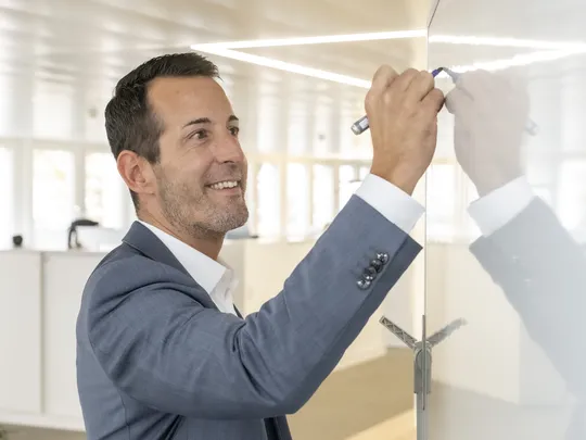 Marco Unterlerchner, an employee of Bosshard & Partner, stands at the whiteboard and writes something on it.
