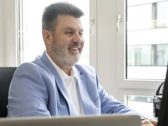 Ralph Becker, an employee at Bosshard & Partner, sits in front of a computer screen and looks at it with a smile.