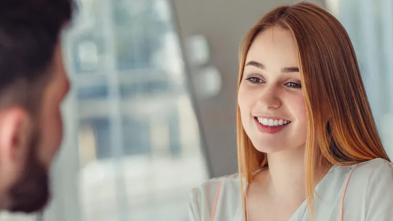 Woman sits opposite a man in a conversation and smiles.