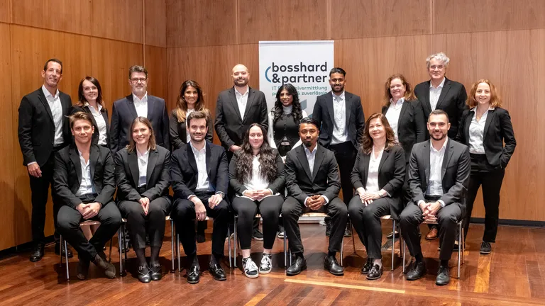 The entire Bosshard & Partner team in two rows, front row seated, back row standing, all in black suits with white blouses or white shirts.