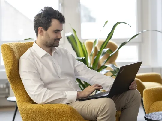 Christian Himmel, an employee of Bosshard & Partner, sits in an armchair and looks at the laptop on his lap.