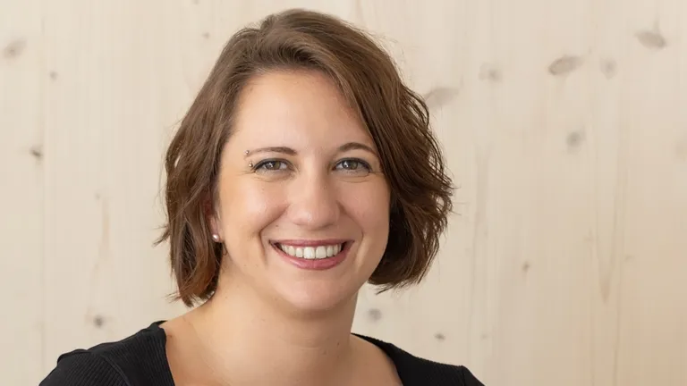Elise Bourgeois, founder of the onyva agency, smiles into the camera against a light-colored wooden background.