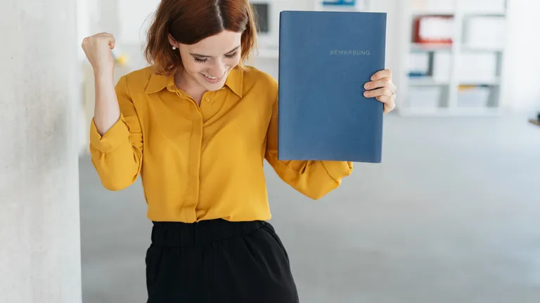 Young woman in a yellow blouse holds a job application folder in her hand and is happy.